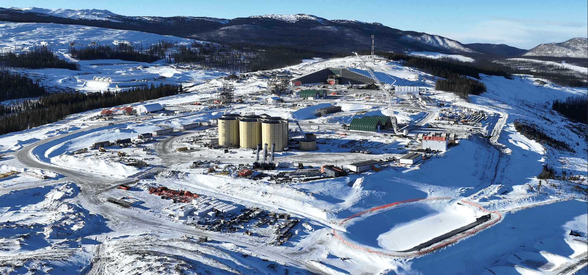 Aerial view of mining complex with processing facilities and forested terrain in BC